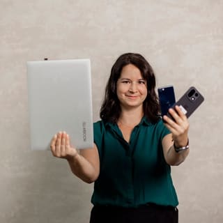 Elisabeth Zeilinger hält in der einen Hand einen Laptop hoch, in der anderen zwei Smartphones.