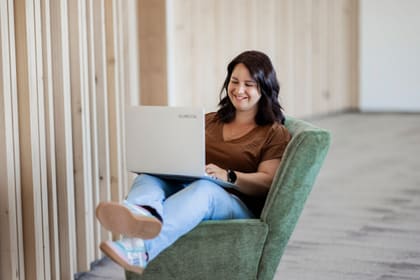 Elisabeth Zeilinger sitting in a green armchair with a laptop on her lap, typing and smiling.